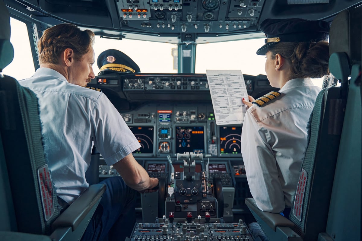 Co-pilot reviewing a pre-flight checklist in the cockpit beside an aircraft captain