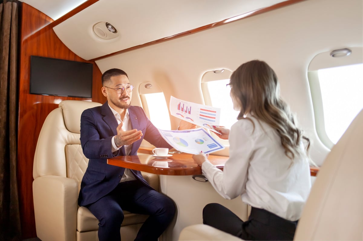 Corporate aviation leadership team reviewing operational diagrams, SOP manuals, and performance dashboards around a conference table in a modern hangar with a business jet visible